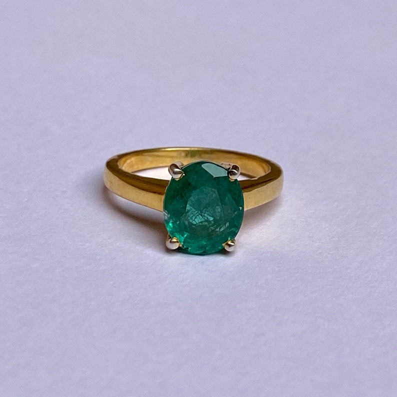 May include: A gold ring with a large, oval-shaped emerald gemstone. The emerald is a deep green color and has a faceted cut.