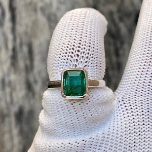 May include: A silver ring with a large, emerald green gemstone set in a square bezel.