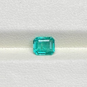 Puede incluir: Una gema de esmeralda verde vibrante cortada en forma cuadrada con bordes biselados.