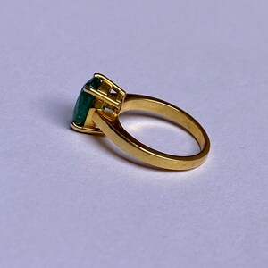 May include: A gold ring with a large, green emerald gemstone set in a prong setting.