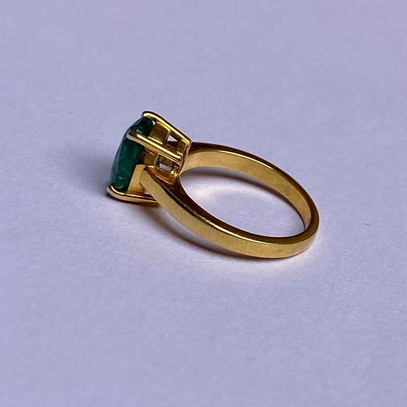 May include: A gold ring with a large, green emerald gemstone set in a prong setting.