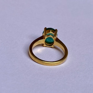 May include: A gold ring with a large oval green gemstone set in a prong setting.