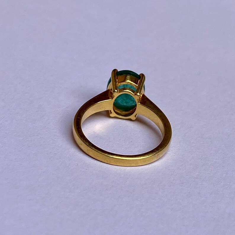 May include: A gold ring with a large oval green gemstone set in a prong setting.