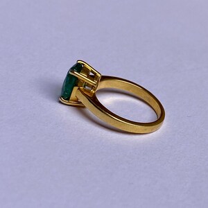 May include: A gold ring with a large, emerald green gemstone set in a prong setting.