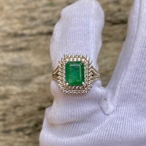May include: A gold ring with a large emerald green gemstone surrounded by a double halo of smaller diamonds.