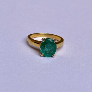 May include: A gold ring with a large, oval-shaped emerald gemstone.