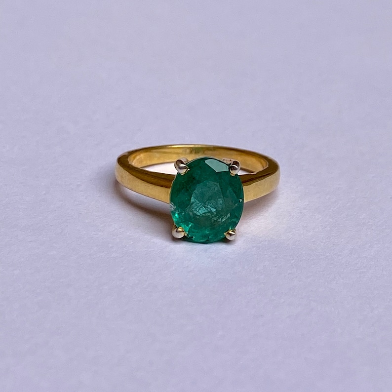 May include: A gold ring with a large, oval-shaped emerald gemstone set in the center. The ring has a simple band and the emerald is a vibrant green color.