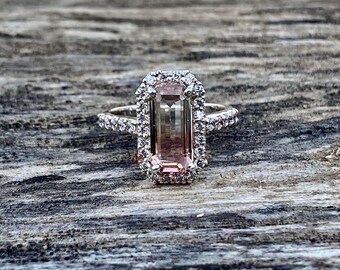 May include: A ring with a large, rectangular, pink and green gemstone surrounded by a halo of smaller diamonds.