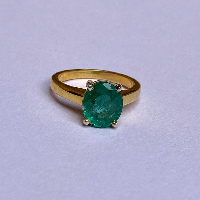 May include: A gold ring with a large, oval-shaped emerald gemstone.
