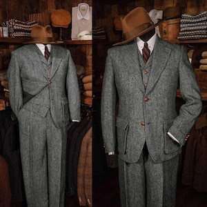 May include: Two gray tweed suits displayed on mannequins. Each suit includes a jacket, vest, and trousers. The jackets have notched lapels and flap pockets. One mannequin wears a brown fedora hat and a striped tie. The suits are displayed in a vintage clothing store.