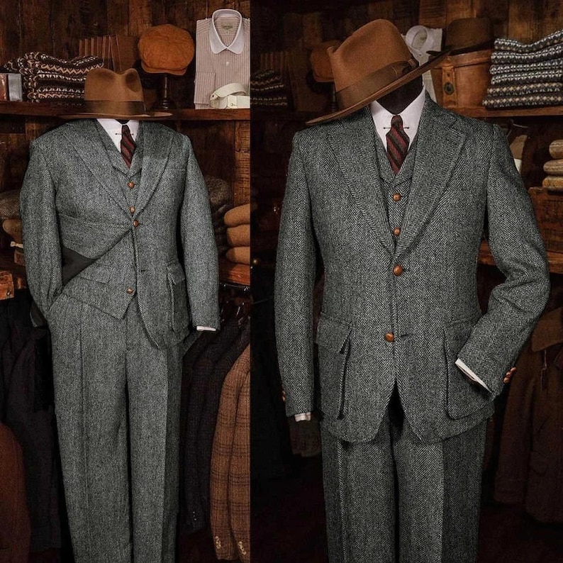 May include: Two gray tweed suits displayed on mannequins. Each suit includes a jacket, vest, and trousers. The jackets have notched lapels and flap pockets. One mannequin wears a brown fedora hat and a striped tie. The suits are displayed in a vintage clothing store.