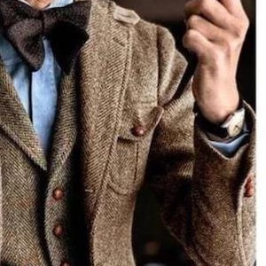 May include: A brown tweed blazer with a matching bow tie. The blazer has a herringbone pattern, brown buttons, and a light blue shirt underneath. The watch on the wrist adds a touch of elegance to the ensemble.