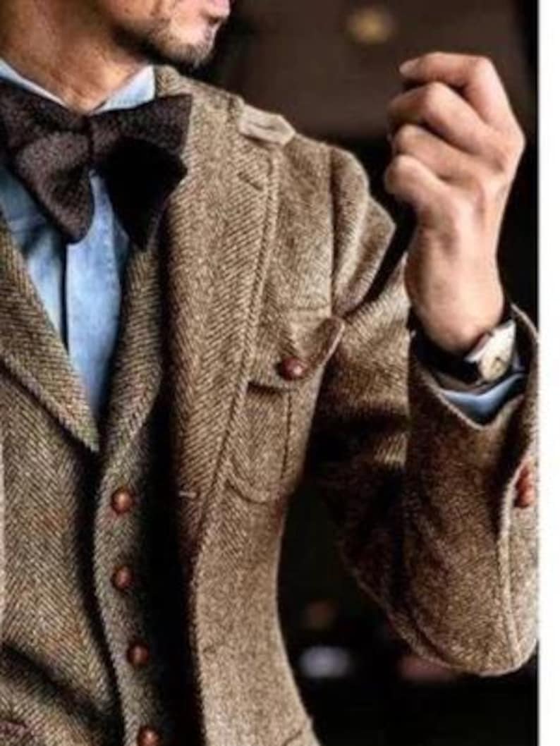May include: A brown tweed blazer with a matching bow tie. The blazer has a herringbone pattern, brown buttons, and a light blue shirt underneath. The watch on the wrist adds a touch of elegance to the ensemble.