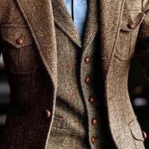 May include: A brown tweed blazer with a matching vest and a light blue shirt. The blazer has two front pockets and brown buttons. The vest has a herringbone pattern. The outfit is a classic style.
