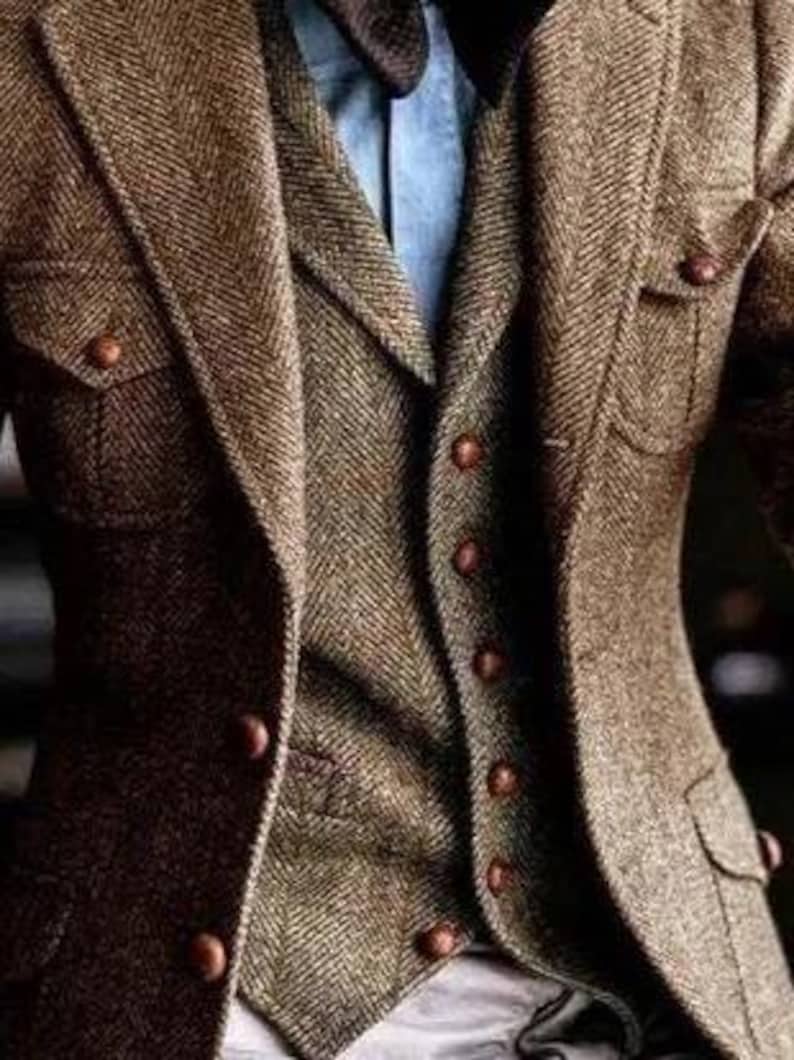 May include: A brown tweed blazer with a matching vest and a light blue shirt. The blazer has two front pockets and brown buttons. The vest has a herringbone pattern. The outfit is a classic style.