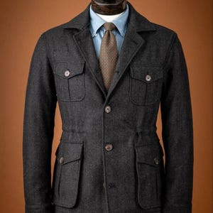 May include: A charcoal gray jacket with four front pockets and button closures. The jacket is worn over a light blue button-down shirt and a patterned tie. The jacket is displayed on a mannequin.