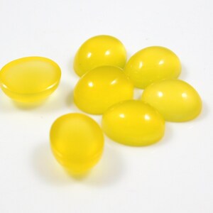 K&ouml;nnte beinhalten: Sieben gelbe Cabochons, oval geformt, auf einer wei&szlig;en Oberfl&auml;che.