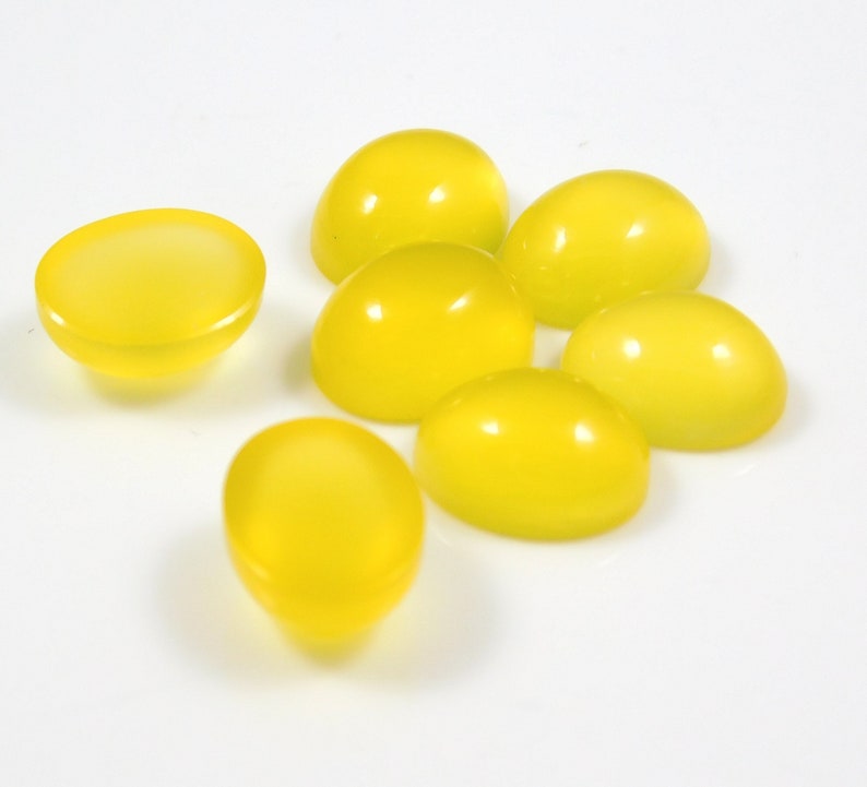 K&ouml;nnte beinhalten: Sieben gelbe Cabochons, oval geformt, auf einer wei&szlig;en Oberfl&auml;che.