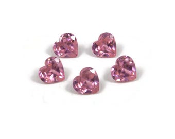 May include: Five pink heart-shaped gemstones on a white background.