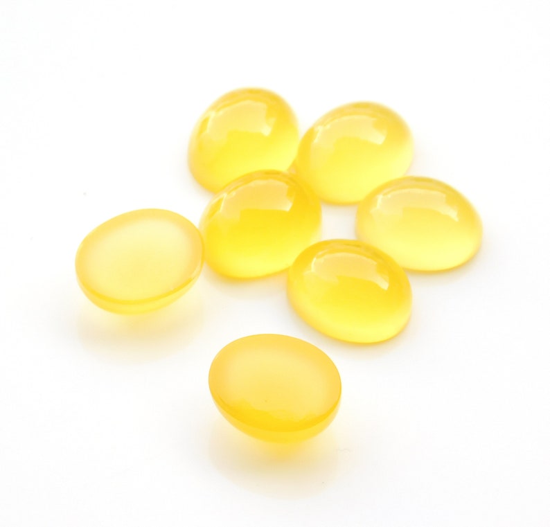 K&ouml;nnte beinhalten: Sieben gelbe ovale Cabochons, auch bekannt als polierte Steine, auf wei&szlig;em Hintergrund.