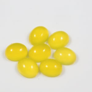 K&ouml;nnte beinhalten: Sieben ovale, gelbe Edelsteine, wahrscheinlich Citrin, in einer lockeren Gruppe auf wei&szlig;em Hintergrund angeordnet.