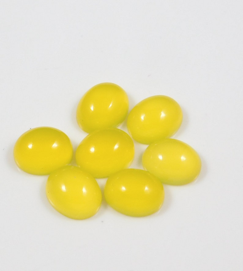 K&ouml;nnte beinhalten: Sieben ovale, gelbe Edelsteine, wahrscheinlich Citrin, in einer lockeren Gruppe auf wei&szlig;em Hintergrund angeordnet.