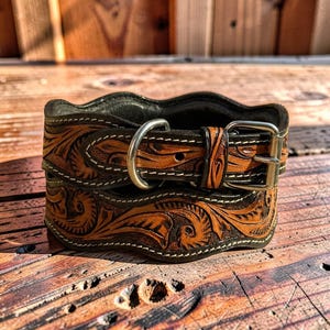 Peut inclure: Un collier de chien en cuir marron et noir avec un outillage floral complexe. Le collier est dot&eacute; d'une boucle et d'un anneau en D argent&eacute;s, et est cousu avec du fil blanc. Le cuir a un bord ondul&eacute;.