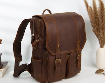 May include: A brown leather backpack with two large front pockets and a zipped closure. The backpack has adjustable straps and a top handle.