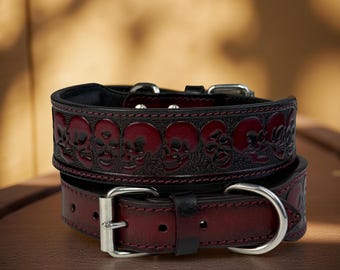 May include: Two leather dog collars. The top collar is black with embossed red skulls. The bottom collar is burgundy with a silver buckle. The collars are stacked on top of each other.