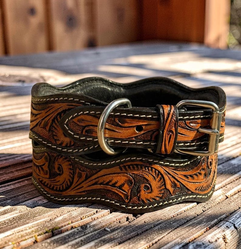 Peut inclure: Un collier de chien en cuir marron et noir, orn&eacute; de motifs floraux complexes. Il est &eacute;quip&eacute; d'une boucle et d'un anneau en D argent&eacute;s, avec des coutures blanches. Le cuir pr&eacute;sente un aspect vieilli naturel. Le collier est pos&eacute; sur une surface en bois.