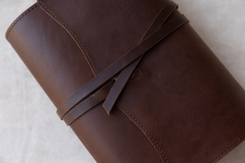 May include: A brown leather journal with a strap closure. The journal has a simple design and is made of high-quality leather.