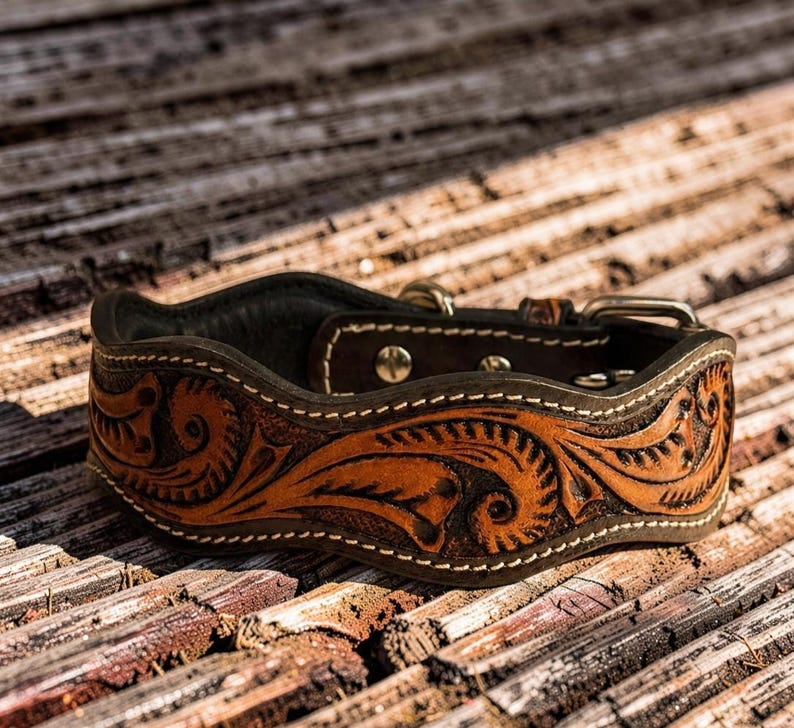 Peut inclure: Un collier de chien en cuir marron avec des motifs floraux complexes. Le collier pr&eacute;sente un int&eacute;rieur marron fonc&eacute; et est orn&eacute; de coutures blanches. Une boucle et une garniture argent&eacute;es compl&egrave;tent le design. Ce collier artisanal est con&ccedil;u pour un chien de taille moyenne &agrave; grande.