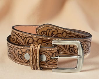 May include: A brown leather belt with a floral embossed design. The belt features a silver-coloured buckle and two silver rivets. The belt is approximately 3.8 cm wide.