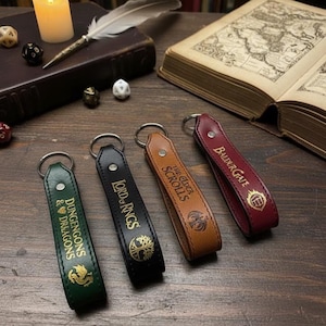 Könnte beinhalten: Vier Leder-Schlüsselanhänger in Grün, Schwarz, Braun und Burgunderrot. Jeder Schlüsselanhänger zeigt ein anderes Fantasy-Thema: Dungeons & Dragons, Der Herr der Ringe, The Elder Scrolls und Baldur's Gate. Die Schlüsselanhänger haben silberne Schlüsselringe.