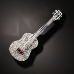 May include: A silver guitar brooch encrusted with sparkling rhinestones and a single red gemstone.