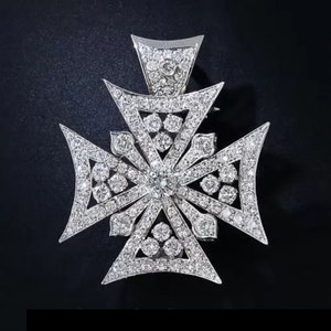 Pode incluir: Um pingente de cruz de prata com um design detalhado de pequenos diamantes. A cruz é um símbolo popular de fé e é frequentemente usada como colar ou broche.