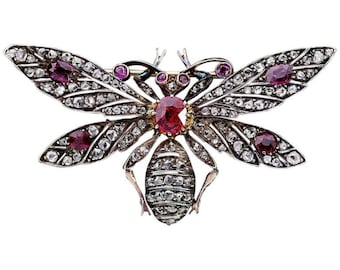 May include: A silver and gold bee brooch with red and white gemstones. The bee's wings are spread and the body is covered in small gemstones.