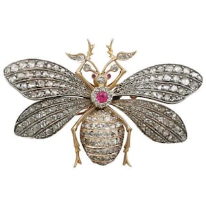 Puede incluir: Un broche de abeja de oro y plata con un centro de rubí y detalles de diamantes.