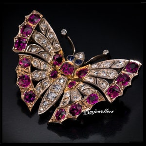 May include: A gold butterfly brooch with ruby and diamond accents. The butterfly's wings are detailed with intricate designs and the body is adorned with a cluster of rubies.