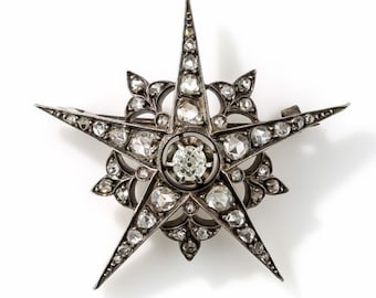 May include: A silver star-shaped brooch with a large, faceted diamond in the center and smaller diamonds set around the edges.