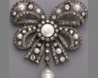 May include: A silver and diamond brooch in the shape of a bow with a large pearl drop pendant. The bow is decorated with smaller pearls and diamonds.
