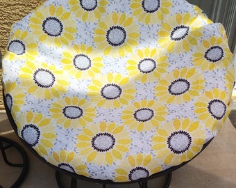 May include: A yellow and gray patterned chair cushion with a sunflower design. The cushion is round and has a black rim.