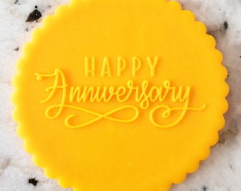 Pode incluir: Um biscoito redondo amarelo com as palavras "Happy Anniversary" em uma fonte cursiva.