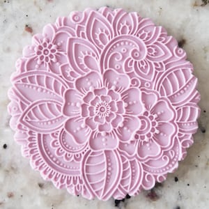 May include: A light purple silicone cake decorating stamp with a detailed floral design. The design features a large flower in the centre surrounded by smaller flowers and leaves.