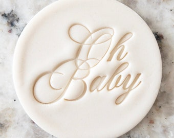 Puede incluir: Cortador de galletas redondo blanco con las palabras "Oh Baby" en letra cursiva.