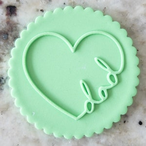 Puede incluir: Una galleta verde claro con un borde festoneado, que presenta una forma de corazón con la palabra "papá" escrita en su interior.