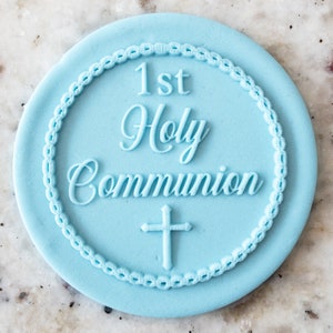 May include: A light blue round cake topper with a white border and the text "1st Holy Communion" and a cross.