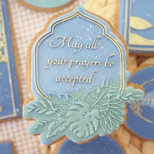 Peut inclure: Un biscuit décoré de bleu et d'or avec le texte "Que toutes vos prières soient acceptées".