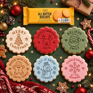 Puede incluir: Seis galletas redondas con bordes festoneados, diseños navideños en relieve y nombres, incluyendo una galleta blanca Merry Christmas, una roja Santa's Favourite Jack, una verde Believe Emily, una beige Baked with Love Smith Family, una azul Let It Snow Thomas y una rosa Christmas at the Browns.
