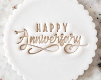 Pode incluir: Cortador de biscoitos redondo branco com borda festonada. O cortador é estampado com o texto "HAPPY Anniversary" em uma fonte cursiva.